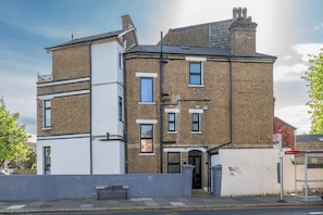 A two-story building with a flat roof, a brick facade, and a white exterior on the lower level. - Chic 1-Bed Apartment in Ealing (London)