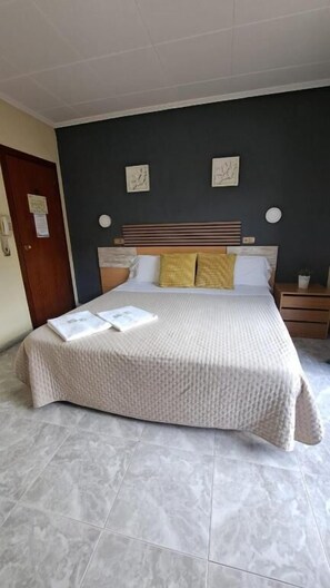A bedroom with a bed, two pillows, a nightstand, and a wall clock. - Hotel Rodsan (Castelldefels)