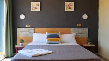 Habitació d'hotel amb llit, dues taules de nit, finestra amb cortines i dues obres d'art penjades a la paret.