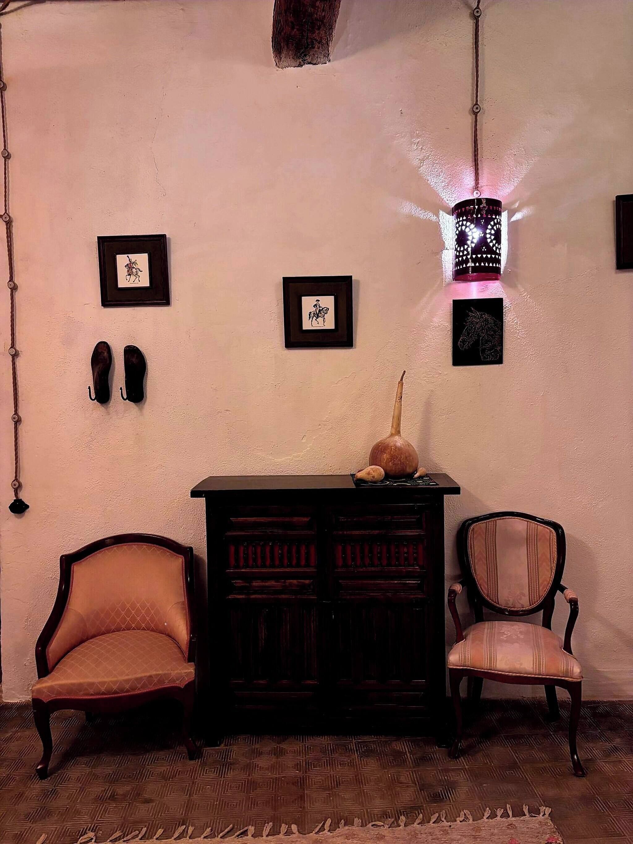 Una habitación con dos sillas, un armario y cuadros en la pared.