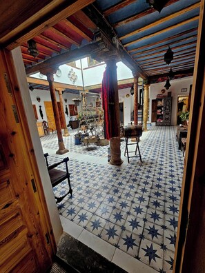 Un interior tradicional con suelo de baldosas, mobiliario de madera y una columna decorativa central.