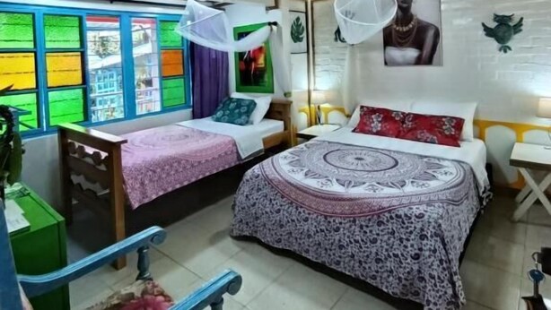 A room with two beds, a wooden ceiling, and a window with colorful views. - San Miguel Filandia 2 (Filandia)