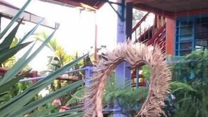 Un banco rojo con cojines amarillos en un jardín con plantas y un edificio colorido al fondo.