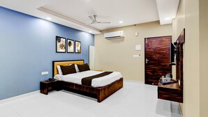 A modern bedroom with a bed, bedside table, ceiling fan, artwork, and an air conditioning unit. - Hotel Fortune Prime (Jaipur)