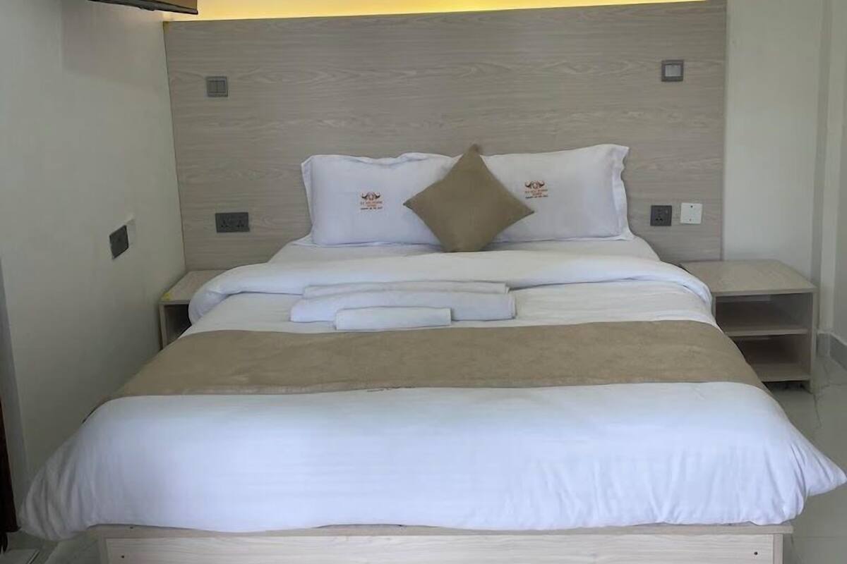A modern bedroom with a bed, bedside tables, a mounted TV, and a wall-mounted light.