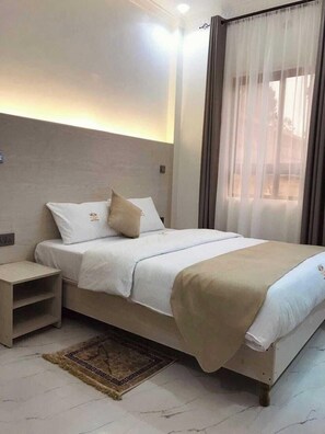 A neatly arranged hotel room with a bed, bedside table, and a window with curtains.