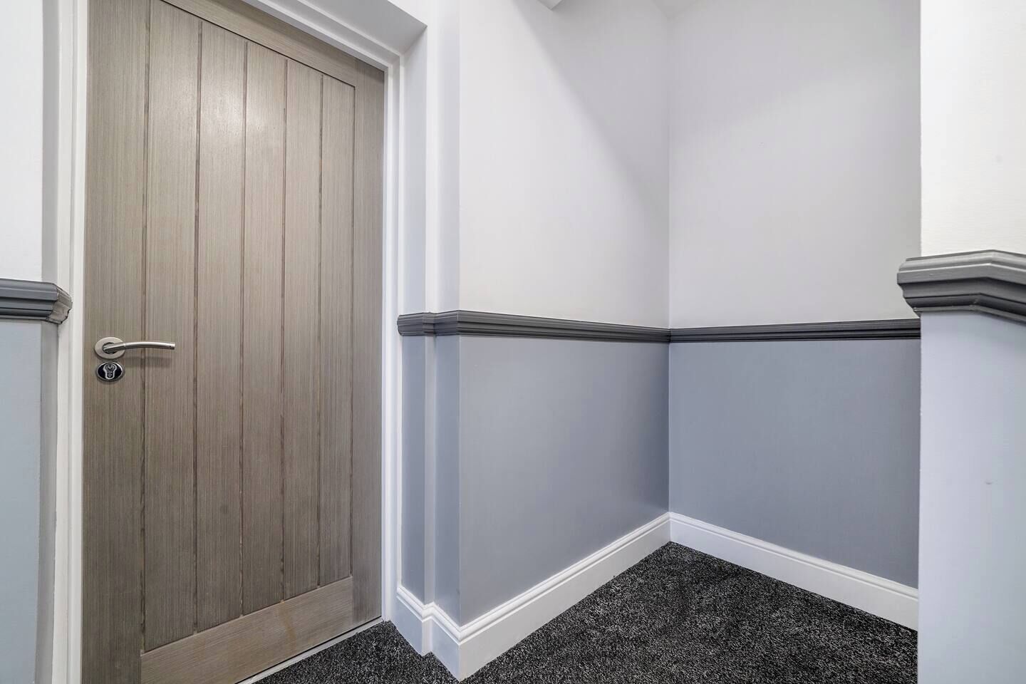 Een hoek van een kamer met een houten deur en een witte muur met donkere sierlijsten.