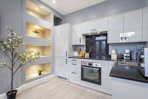 Une cuisine moderne avec des meubles blancs, un four encastré et un plan de travail noir.