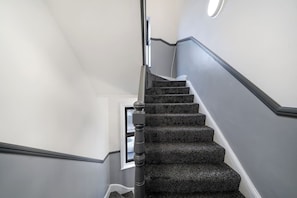 A staircase with a handrail, carpeted steps, and a door at the bottom. - Stunning 1 Bedroom Apartment (London)