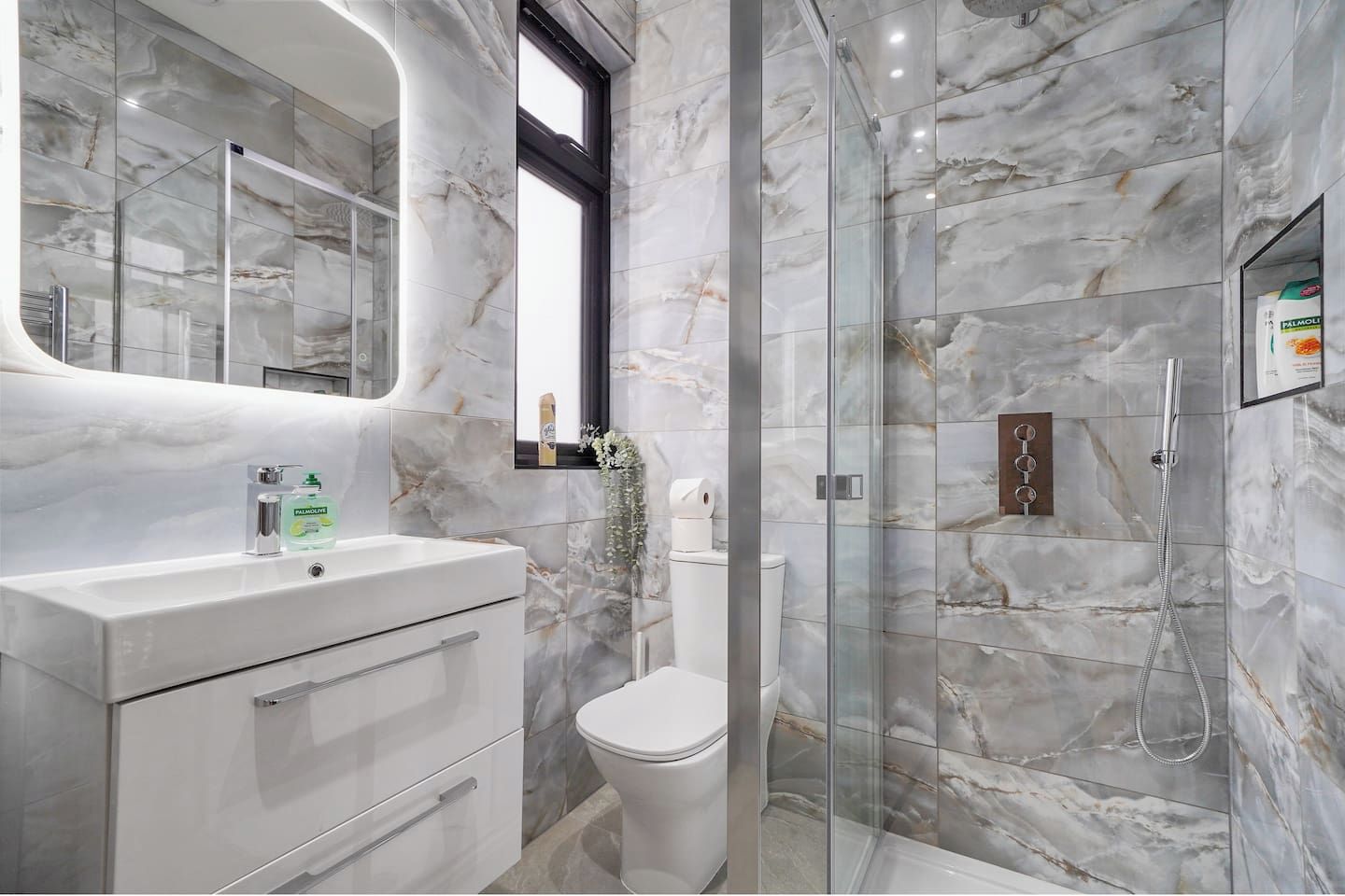 A modern bathroom with a marble wall, a glass shower enclosure, a white toilet, and a vanity with a mirror.