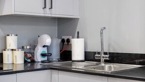 Eine moderne Küche mit weißen Schränken, einer Edelstahlspüle und verschiedenen Geräten, darunter eine Kaffeemaschine und ein Wasserkocher.