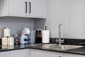 Eine moderne Küche mit weißen Schränken, einer Edelstahlspüle und verschiedenen Geräten, darunter eine Kaffeemaschine und ein Wasserkocher.