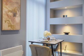 Un espace repas moderne avec une table dressée pour deux personnes, un vase décoratif rempli de fleurs et une étagère minimaliste agrémentée d’un bol et de bougies.