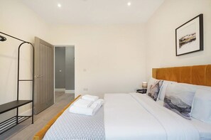 Una habitación de hotel con una cama, un banco, un armario y un cuadro en la pared.