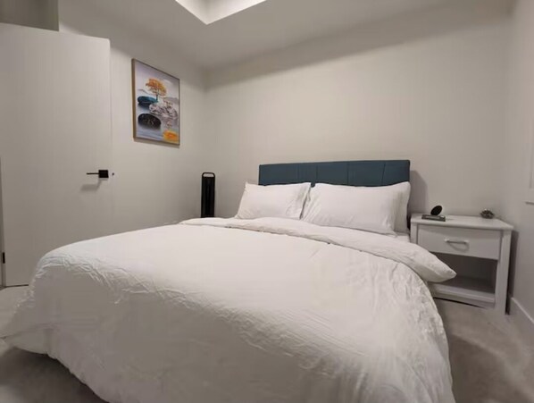 Ein Schlafzimmer mit einem Bett, einem Nachttisch, einer Tür und einem an der Wand befestigten Kunstwerk.