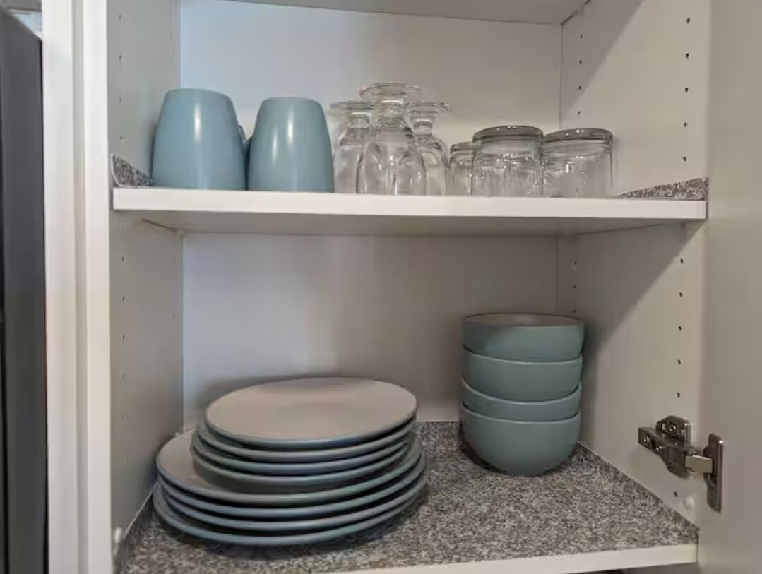 A kitchen cabinet with shelves holding plates, bowls, and glass jars.