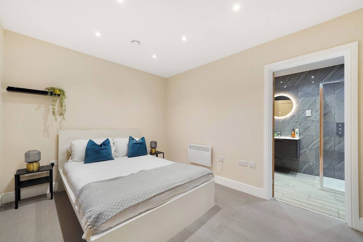 Un dormitorio moderno con cama, mesitas de noche, radiador y baño con pared de mármol y espejo circular.