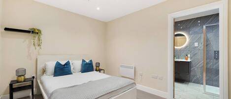 Un dormitorio moderno con cama, mesitas de noche, radiador y baño con pared de mármol y espejo circular.