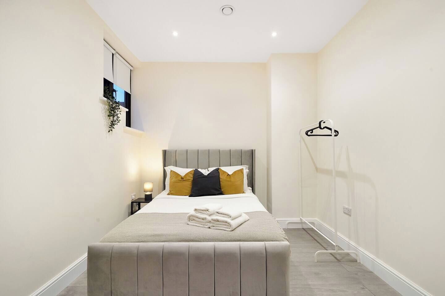 A hotel room with a bed, bedside table, lamp, and a hanging coat rack.