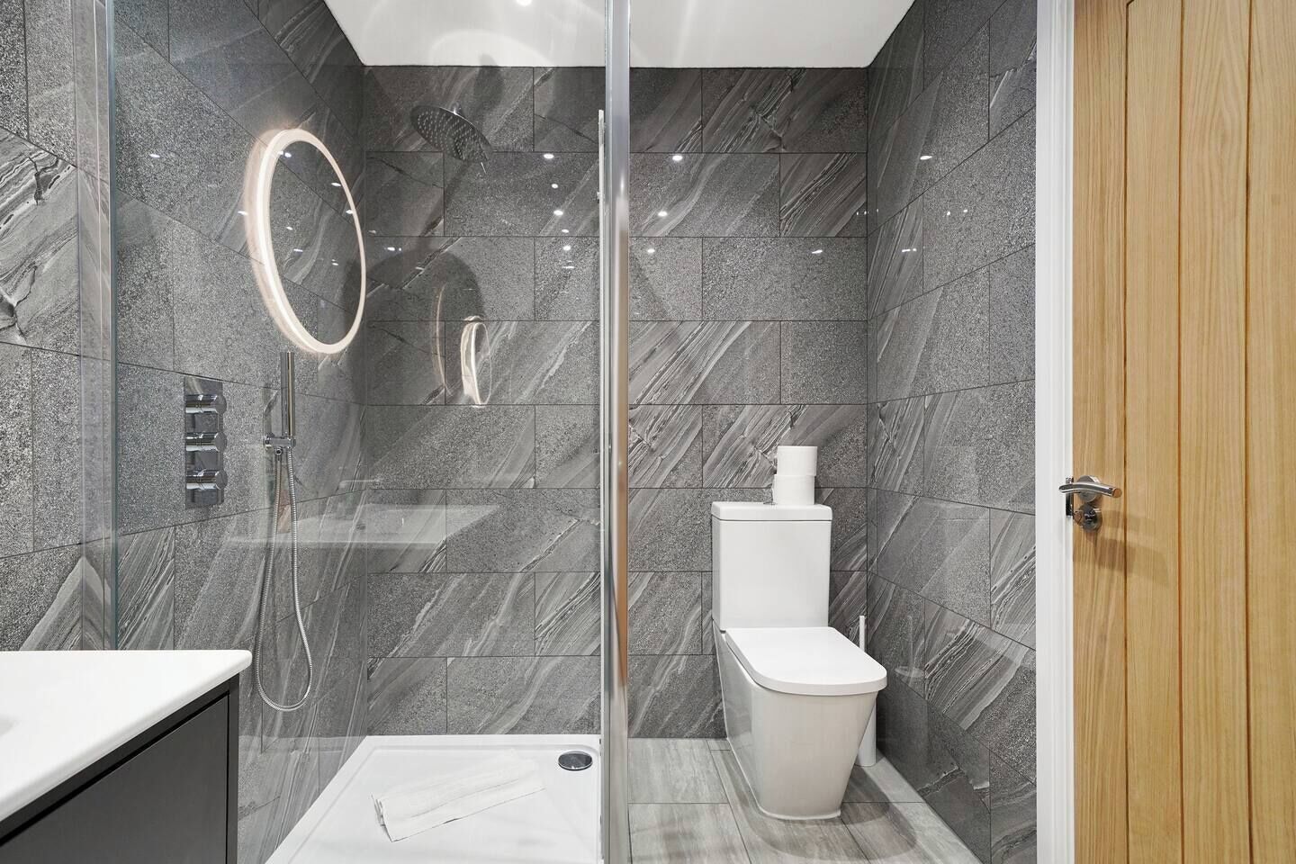 Een moderne badkamer met een glazen douchecabine, toilet en wastafel.