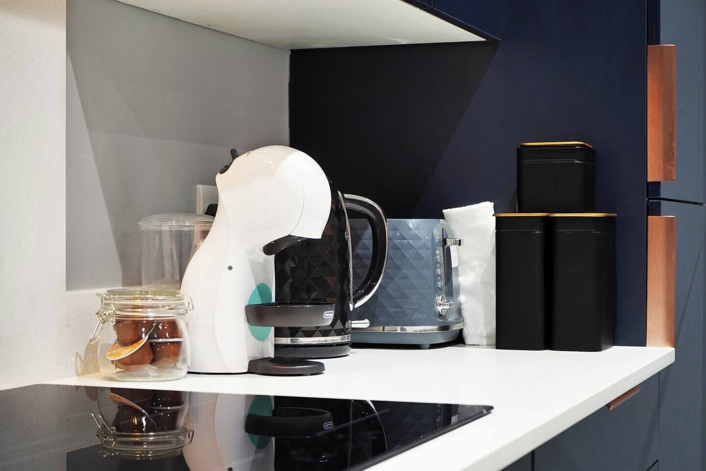 Una encimera de cocina con una cafetera, un tarro de vidrio y un electrodoméstico negro.