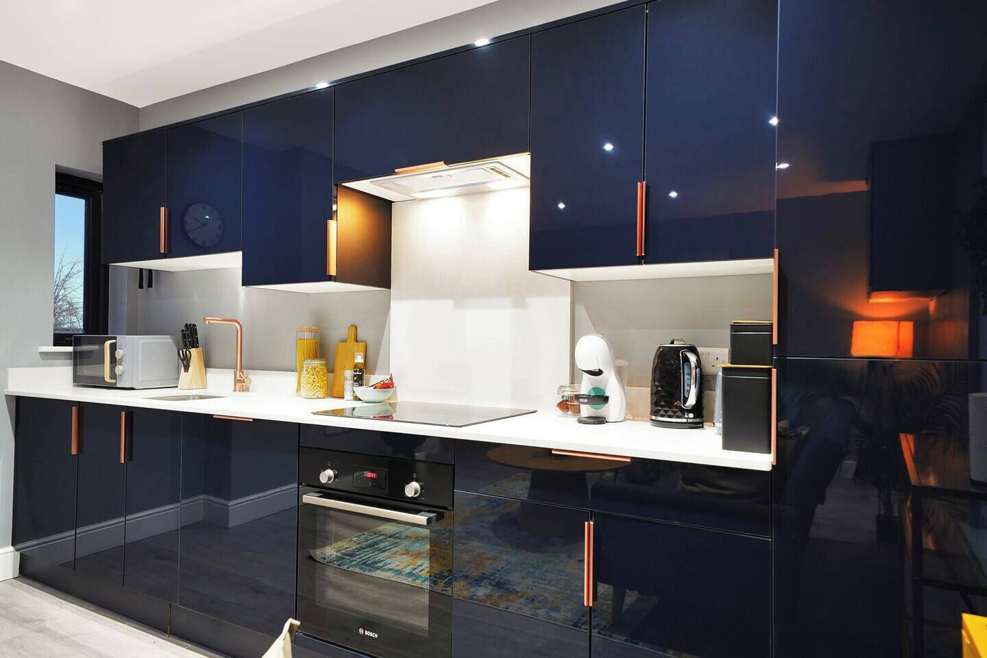 A modern kitchen with dark cabinetry, a white countertop, and various appliances including a microwave, toaster, and coffee maker.