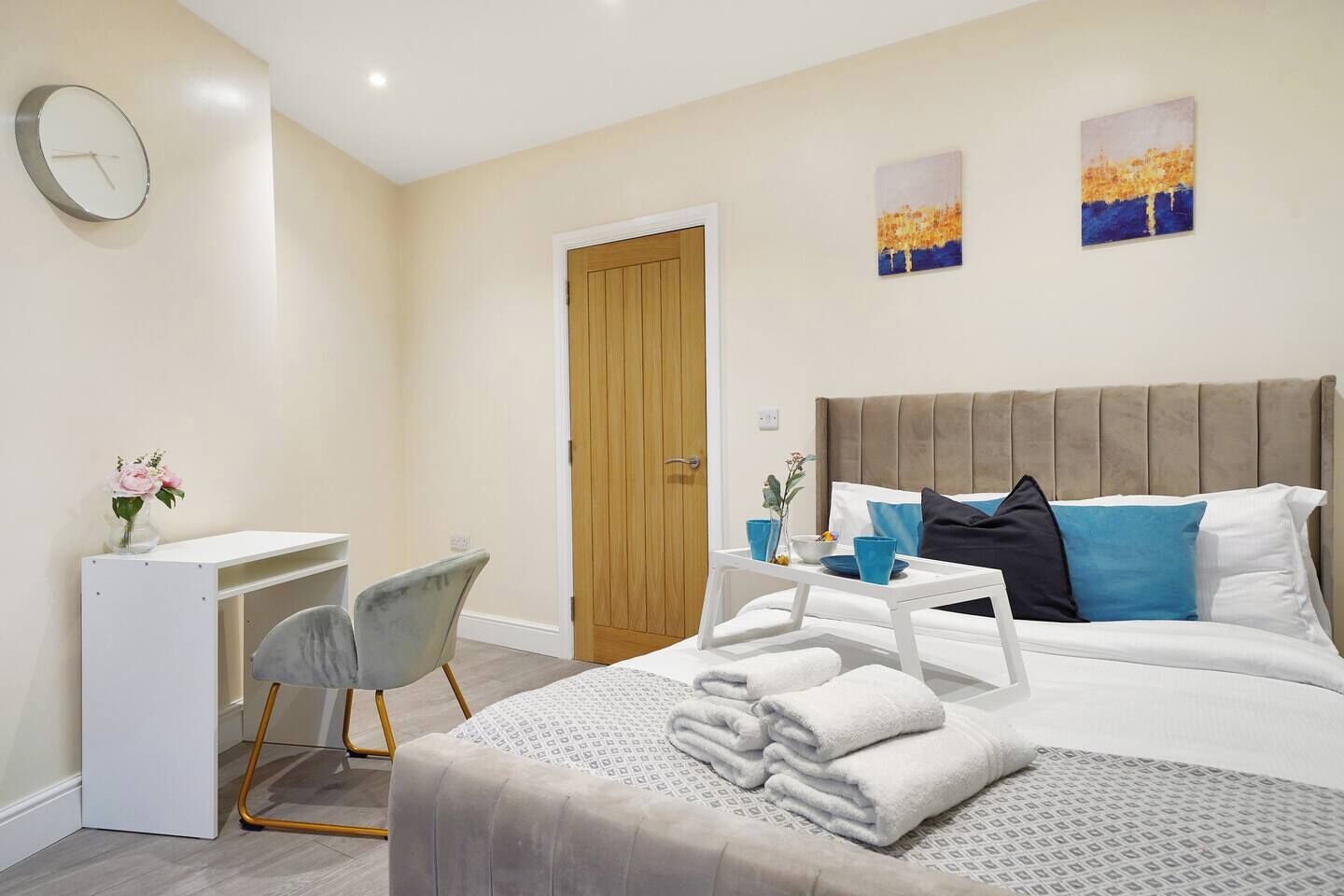 A hotel room with a bed, bedside table, chair, desk, and artwork on the walls.