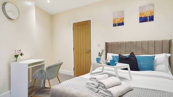 A hotel room with a bed, bedside table, chair, desk, and artwork on the walls.