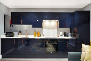 A modern kitchen with dark cabinets, a white countertop, and stainless steel appliances. - Modern & Cozy 3-Bed Apartment (London)
