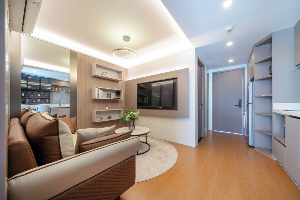A modern living room with a sofa, a TV mounted on the wall, and a kitchen area in the background.
