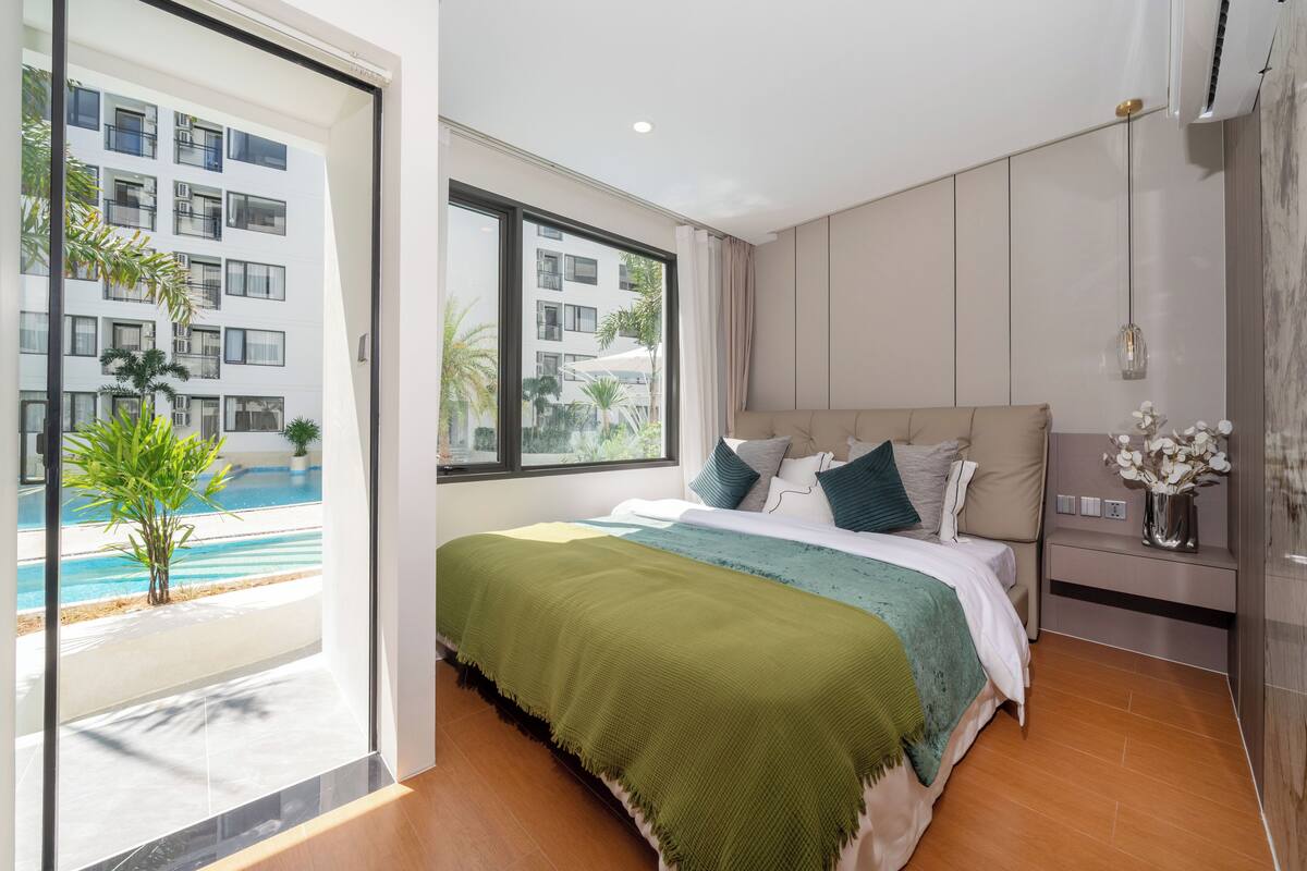 A modern bedroom with a large bed, a view of a swimming pool, and a sliding glass door.