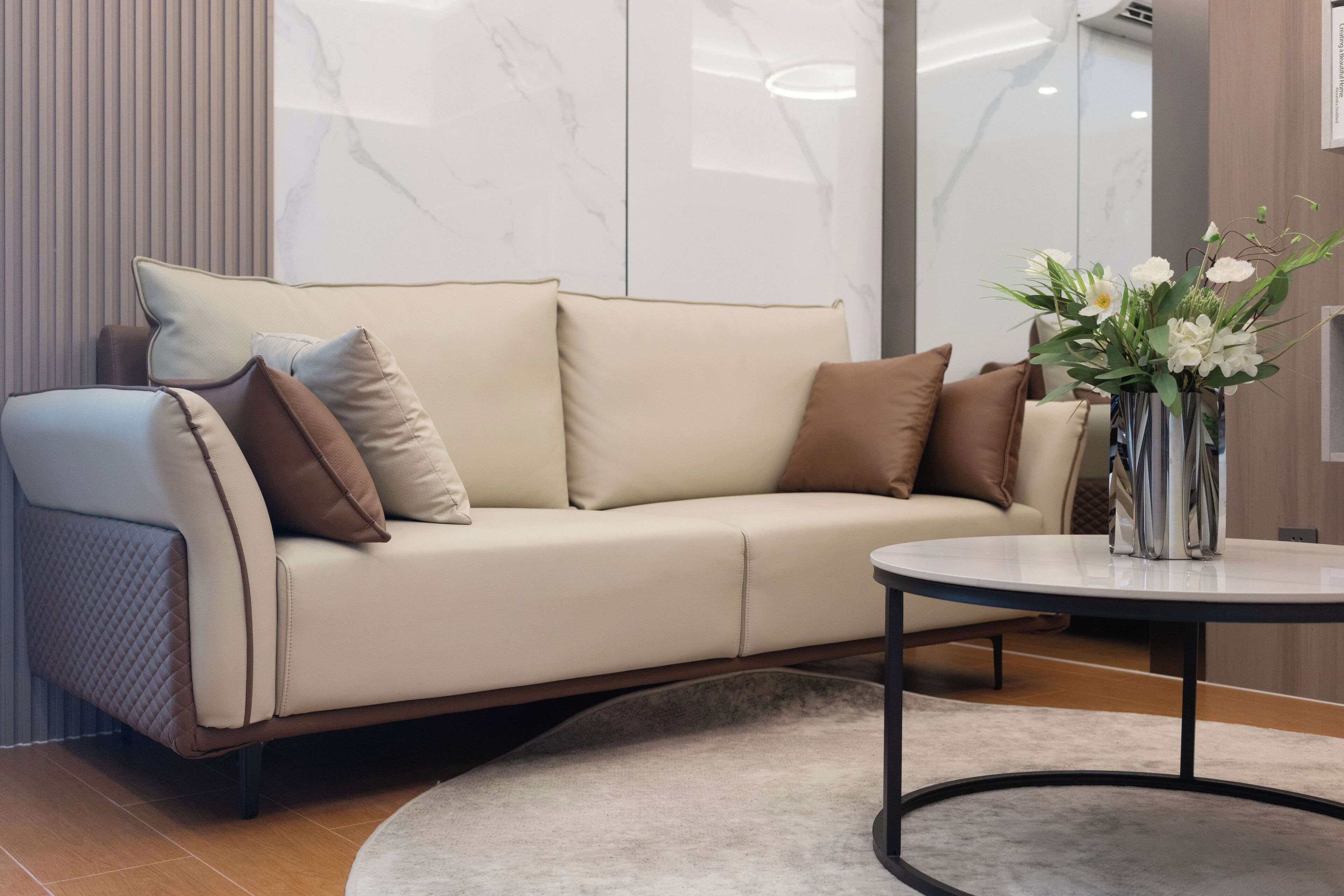 A modern living room with a beige sofa, a round coffee table, and a vase of white flowers.