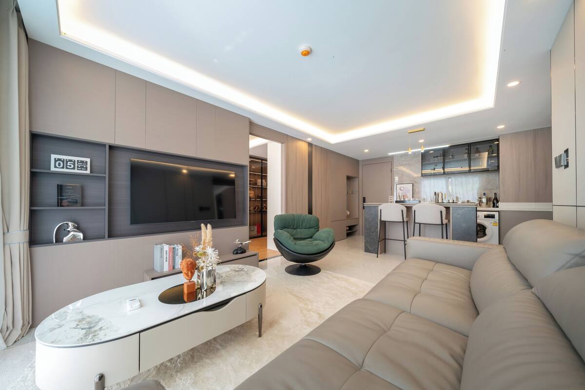 Ein modernes Wohnzimmer mit einer Couch, einem grünen Sessel, einem Fernseher und einer Küchenzeile.
