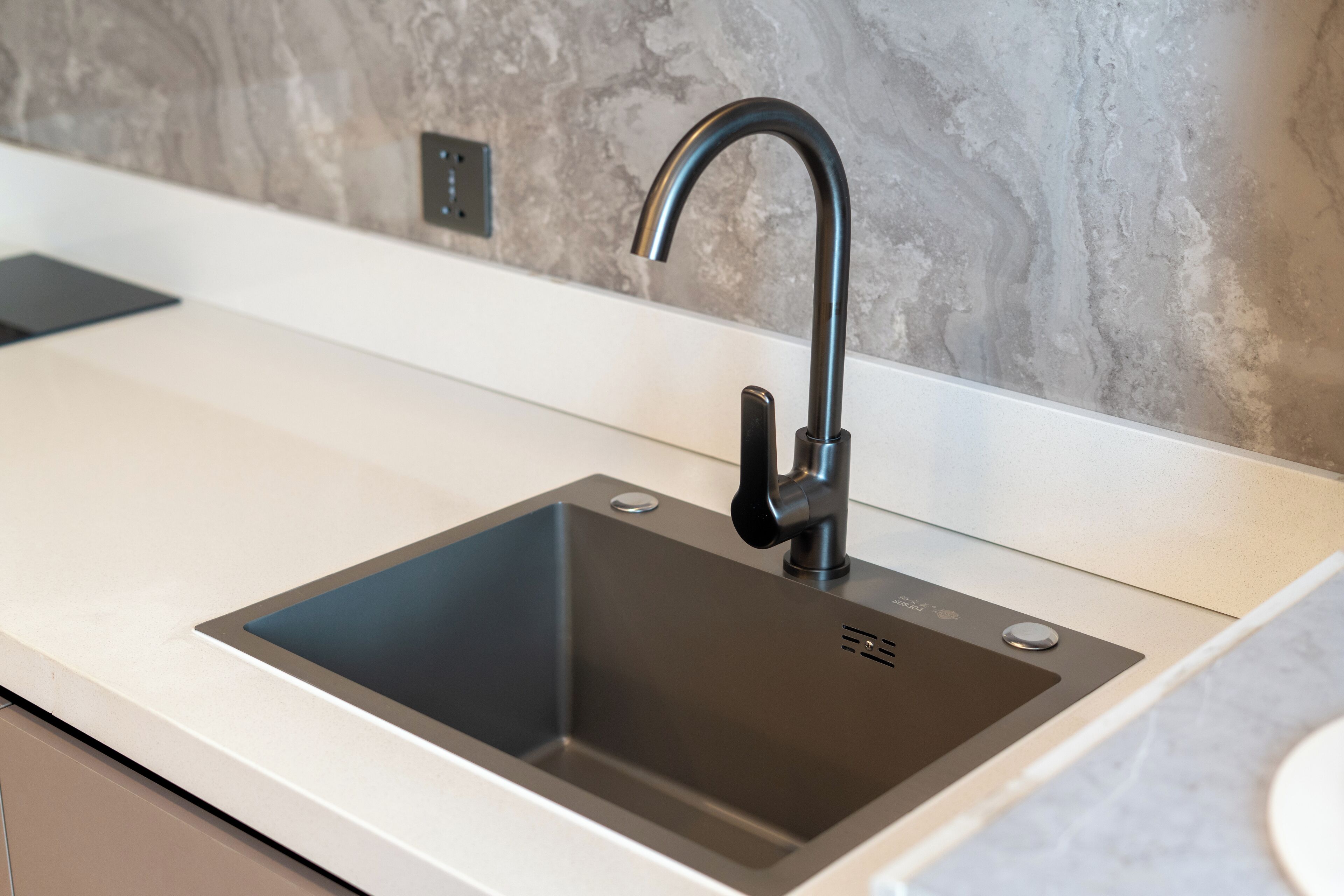 A modern kitchen with a sleek black sink, a marble backsplash, and a minimalist countertop.