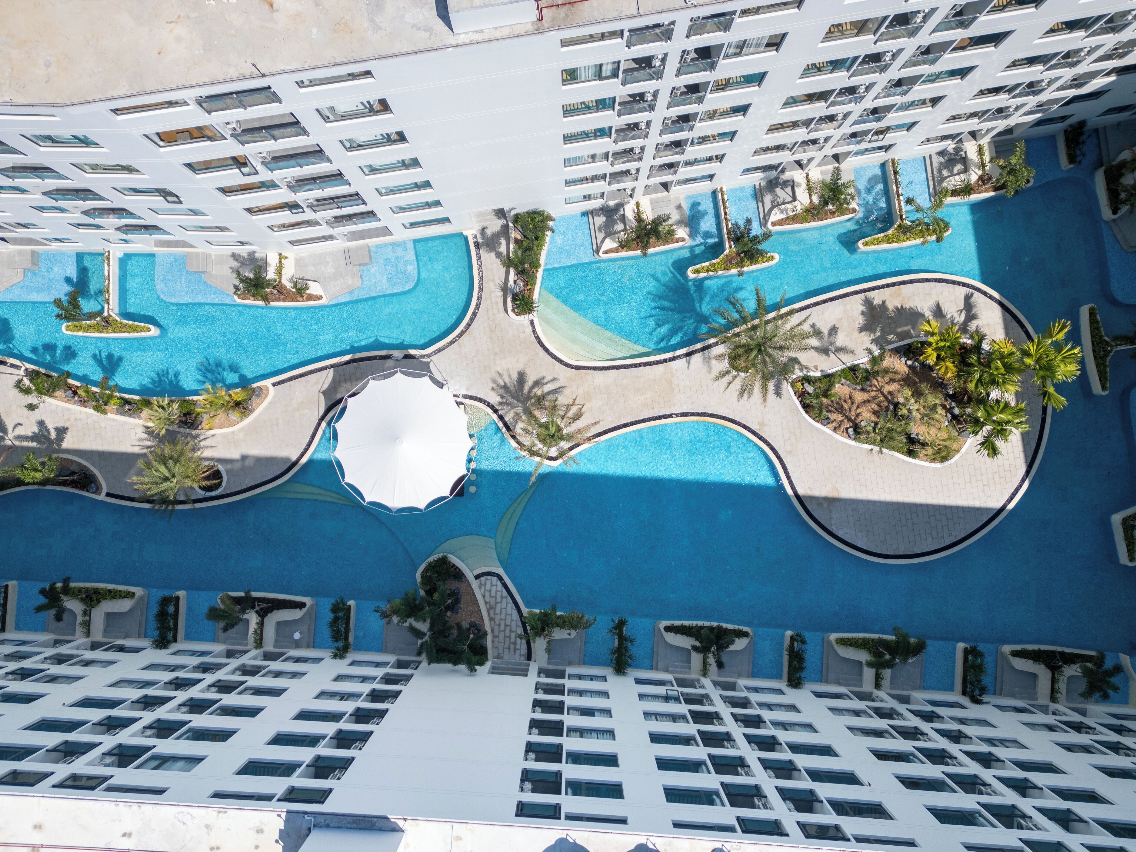 Un hotel moderno con numerosi balconi, una piscina centrale e aree verdi circostanti.