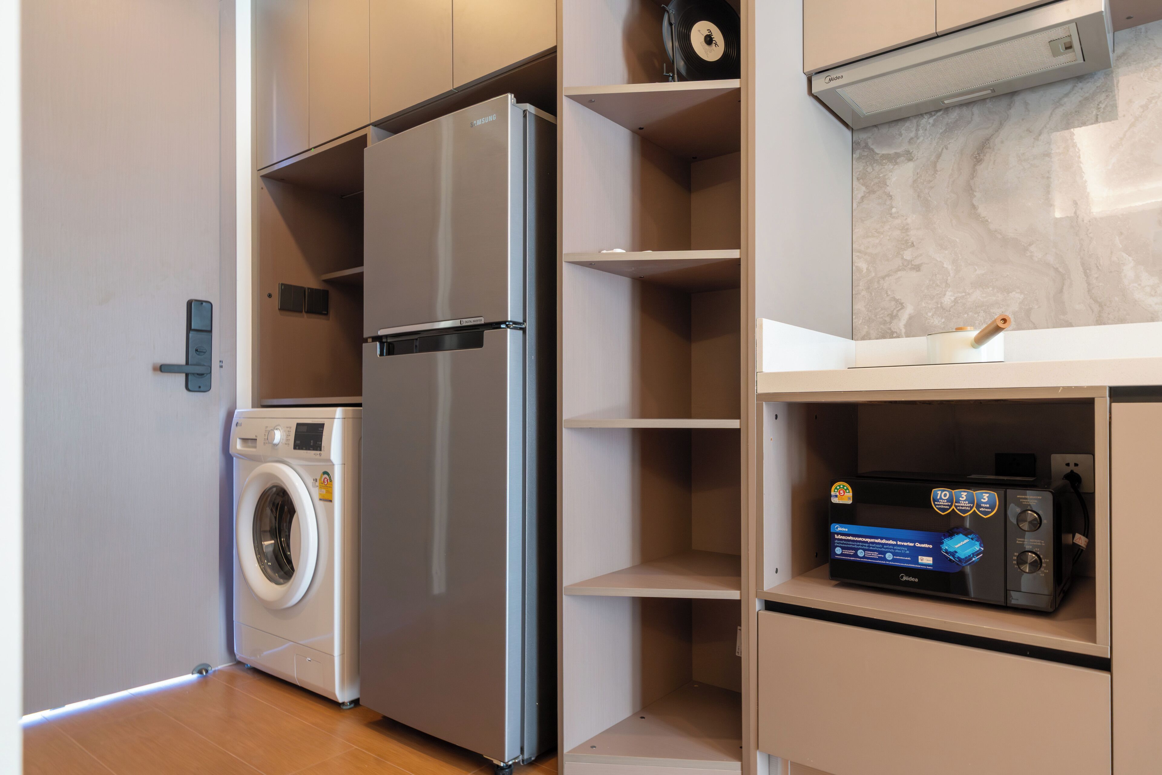 A compact kitchen with a stainless steel refrigerator, a built-in washing machine, and a microwave on a shelf.
