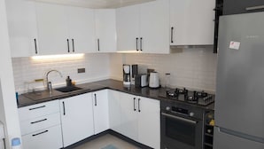 A modern kitchen with white cabinets, a black countertop, a Bosch refrigerator, a coffee maker, and an oven.