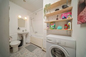 A compact bathroom with a toilet, sink, shower, and a washing machine. - Cosy 2 Bed Flat in Naujamiestis (Luton)