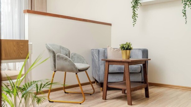 A room with a grey upholstered chair, a small wooden table with a potted plant, and a grey sofa. - Cosy 2 Bed Flat in Naujamiestis (Luton)