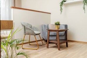 Ein Zimmer mit grauem Polstersessel, einem kleinen Holztisch mit Topfpflanze und einem grauen Sofa.