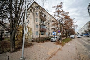 A multi-story residential building with a pedestrian crossing sign, parked cars, and a sidewalk. - Cosy 2 Bed Flat in Naujamiestis (Luton)