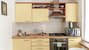 A compact kitchen with a gas stove, microwave, and a small dining area. - Cosy 2 Bed Flat in Naujamiestis (Luton)