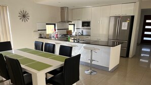 Una cucina moderna con mobili bianchi, un frigorifero in acciaio inossidabile e un'area pranzo con tavolo bianco e sedie nere.