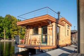 A wooden cabin with a balcony, a ladder, and a dock extending into a body of water.
