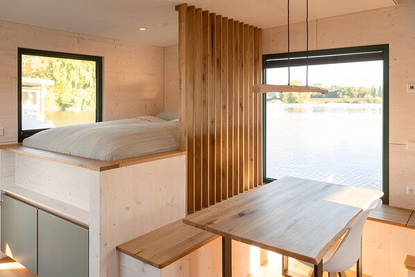 A modern room with a bed, a wooden slat partition, a table, and a view of a body of water.