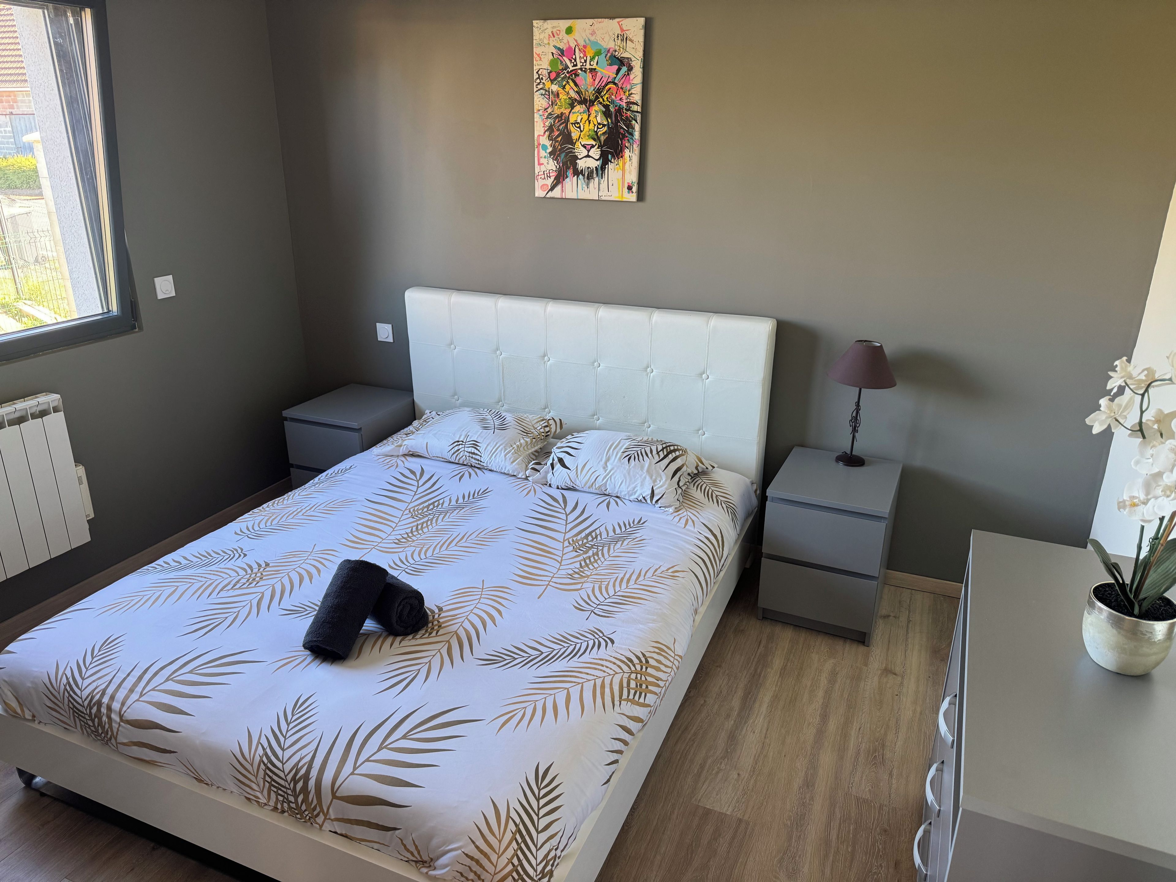 Een slaapkamer met een bed, nachtkastjes, een radiator, een kunstwerk aan de muur en een potplant.
