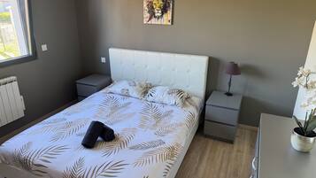 Een slaapkamer met een bed, nachtkastjes, een radiator, een kunstwerk aan de muur en een potplant.