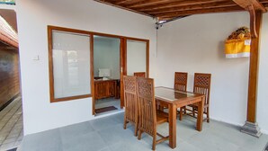 A covered patio with a wooden table and chairs, a sliding glass door, and a small desk with a lamp. - Aming Villa Balangan (Jimbaran)