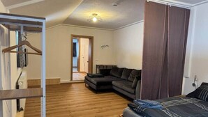 Een kamer met een houten vloer, een bank, een bed met een gestreept deken en een deur naar een andere kamer.