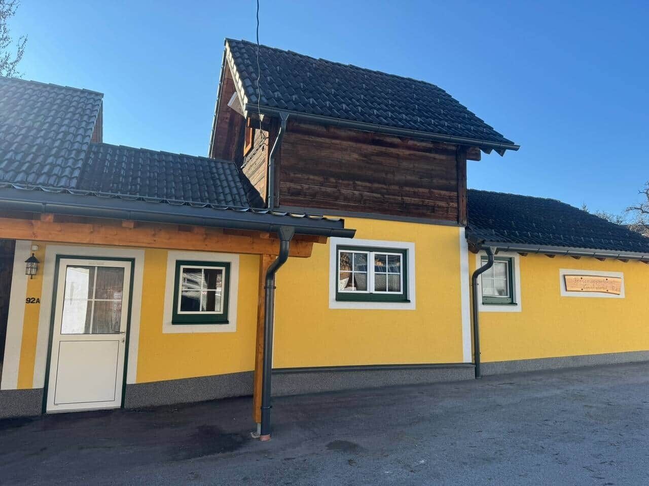 A yellow building with a wooden upper section, a door, and windows.